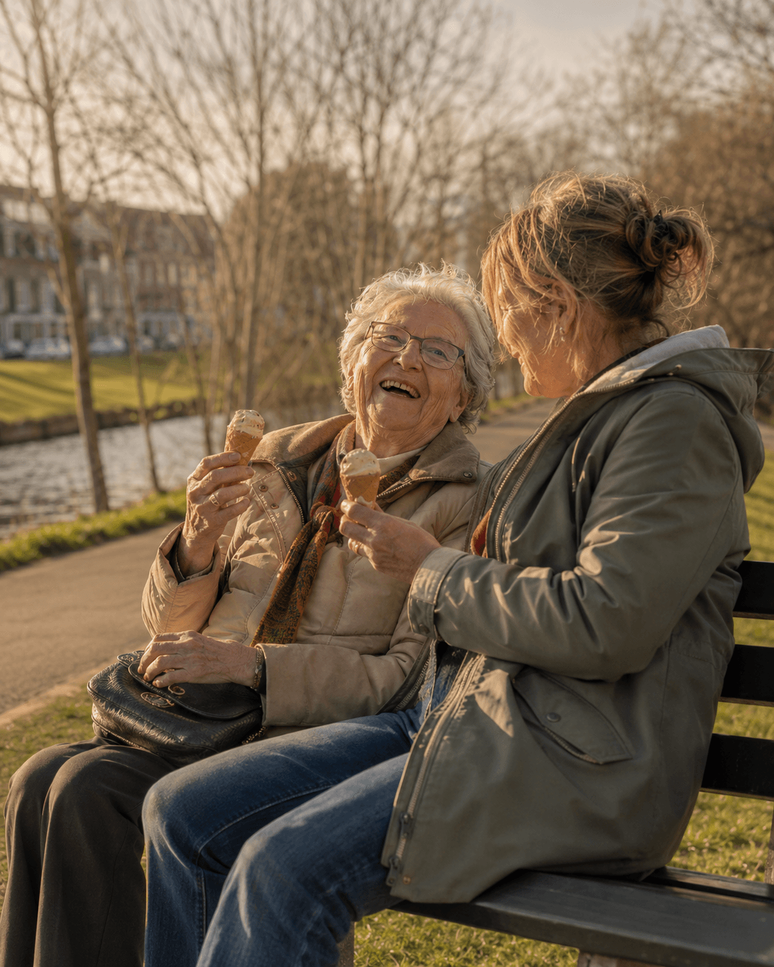 Een dochter en haar moeder lachen samen op een bankje langs het water, allebei met een ijsje.